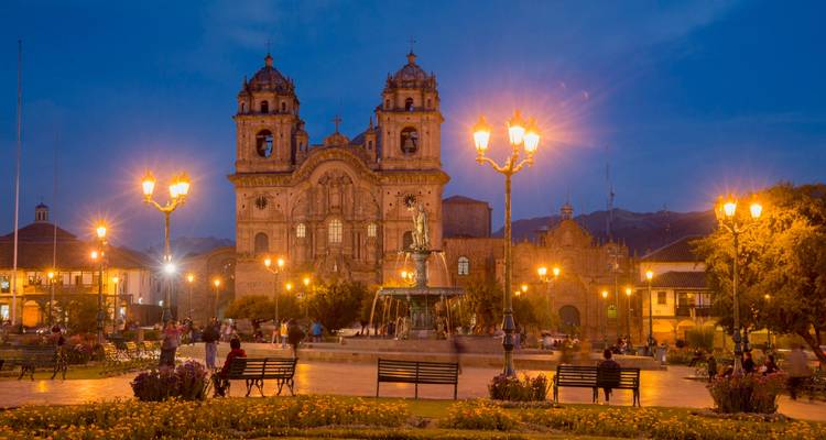Evening lights illuminate Plaza de Armas and Cusco Cathedral under deep blue sky.