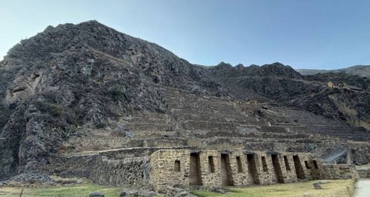 Ruins of Ollantaytambo terraces built into dark rocky hillside under clear sky.