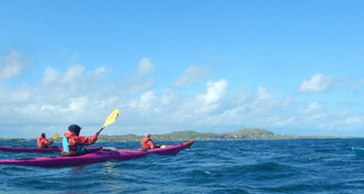 Los kayakistas con equipo rojo reman a través de aguas azules agitadas bajo un cielo amplio y abierto.