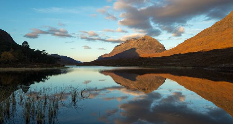 Un pico montañoso se refleja perfectamente en las aguas quietas de un lago a la hora dorada con luz cálida en las laderas.