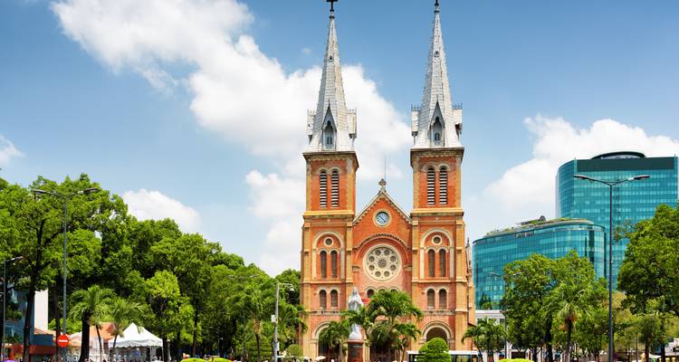 Neoromanische Backsteinkathedrale mit Zwillingstürmen, eingerahmt von Bäumen unter strahlend blauem Himmel