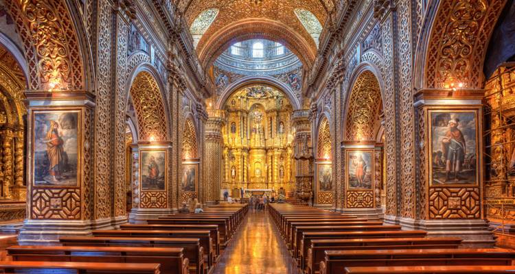 Lavishly gilded interior of a baroque church with long wooden pews and ornate arches.