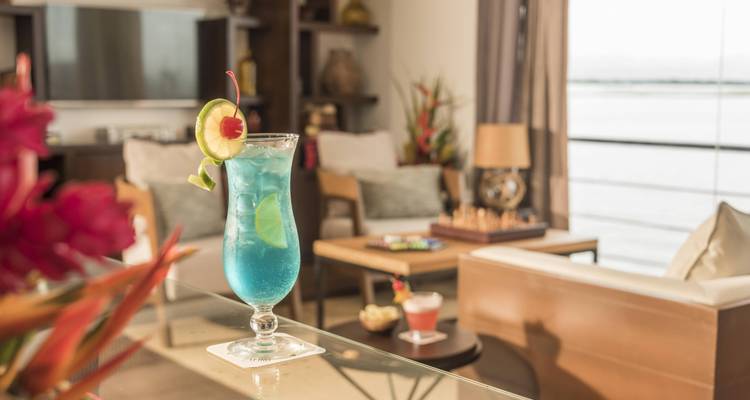 Ein lebendiger blauer Cocktail, garniert mit Limette und Kirsche, steht auf einem Glastisch in einer eleganten Lounge.