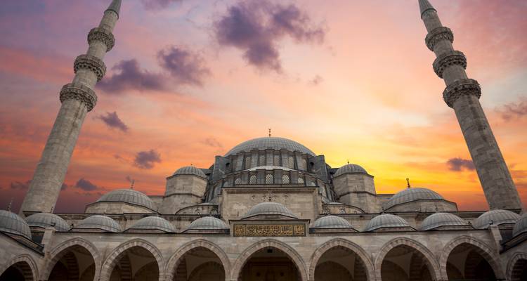 Frontansicht einer prächtigen Istanbuler Moschee, die sich gegen einen leuchtend orangefarbenen Sonnenuntergangshimmel abzeichnet.
