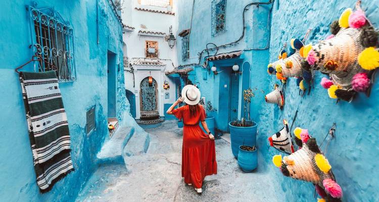 Mujer con vestido rojo y sombrero pasea por los vibrantes callejones azules de Chefchaouen.