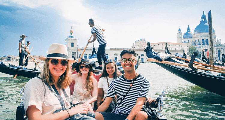A group of friends enjoy a gondola ride on Venice’s canals with historic domes behind.