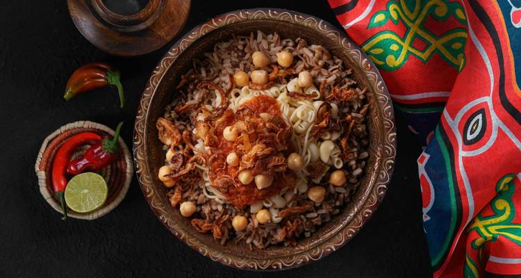 Vogelperspektive eines traditionellen ägyptischen Koshari-Gerichts garniert mit Kichererbsen und knusprigen Zwiebeln auf einem dunklen Tisch.