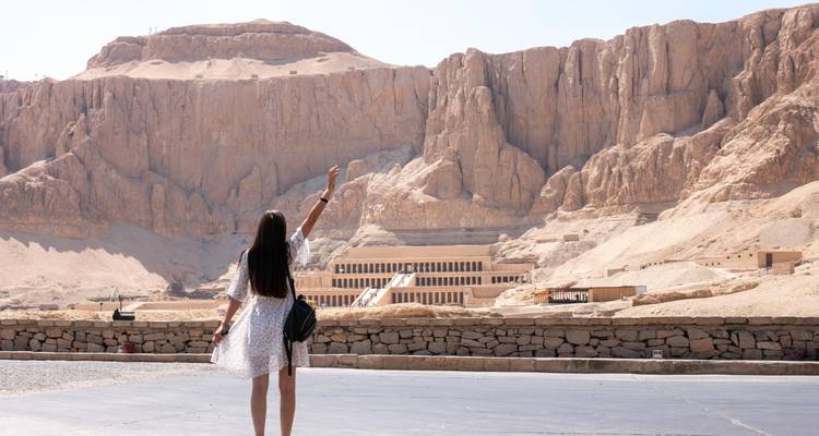 Besucher zeigt auf die in die Klippen von Deir el-Bahari gehauenen Tempelterrassen in Luxors Wüstenlandschaft.