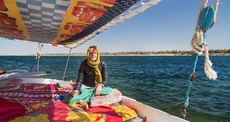 Ein weiterer Blickwinkel auf einen Reisenden, der sich auf bunten Kissen an Bord einer Feluke entspannt, die auf dem Nil segelt.