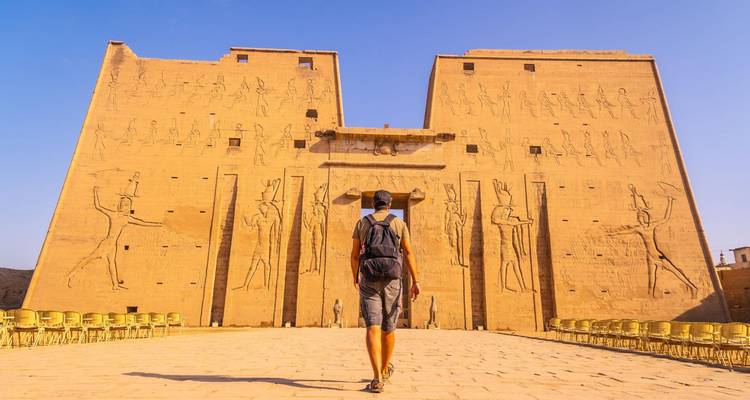 Reisender steht vor den imposanten reliefverzierten Mauern des Edfu-Tempels im hellen Nachmittagslicht.