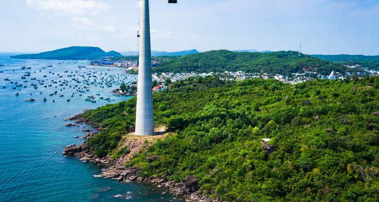 Luchtfoto van groene eilandkustlijn met een hoge kabelbaan-mast die boven de zee uitrijst