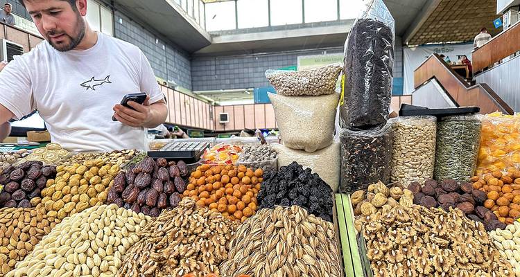 Market vendor selling assorted nuts, dried fruit and grains at an indoor bazaar counter.