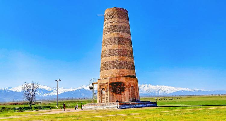Historic Burana Tower rising from flat grassland with snowy peaks on the horizon.