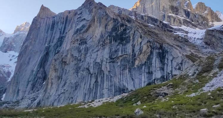 Paroi de granit imposante striée de neige s'élevant au-dessus d'une prairie alpine.