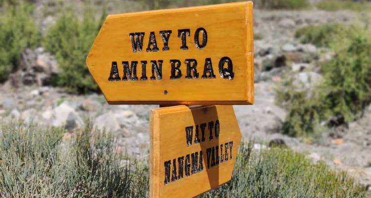 Gros plan de panneaux de sentier en bois jaunes pointant vers Amin Brak et la vallée de Langar.