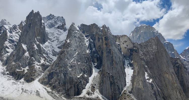 Gamme rapprochée de pics de granit accidentés drapés de neige sous des nuages fragmentés.