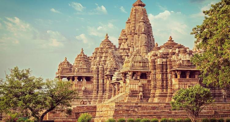 Großer westlicher Gruppentempel in Khajuraho, der sich inmitten von Grün unter pastellfarbenem Himmel erhebt.