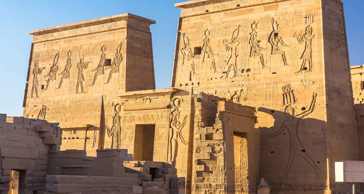 Muros de arenisca del Templo de Filae con relieves jeroglíficos detallados iluminados por el cálido sol de la tarde.