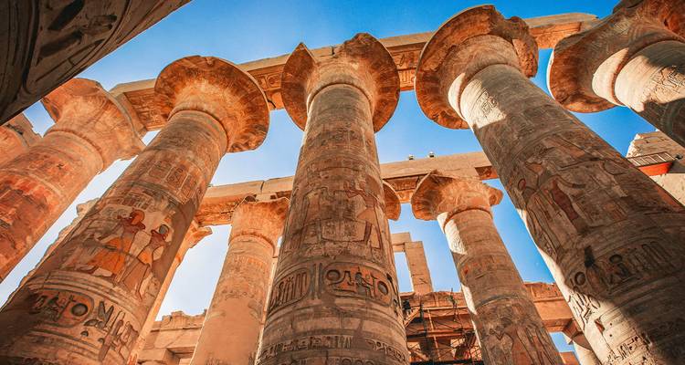 Mirando hacia las imponentes columnas del Templo de Karnak con jeroglíficos vívidos contra un cielo azul brillante.