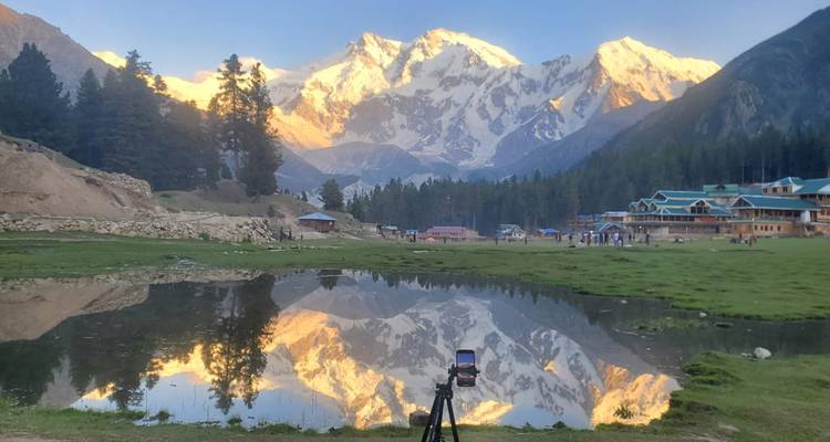 Le Nanga Parbat doré se reflète dans un étang immobile avec un appareil photo sur trépied au premier plan.