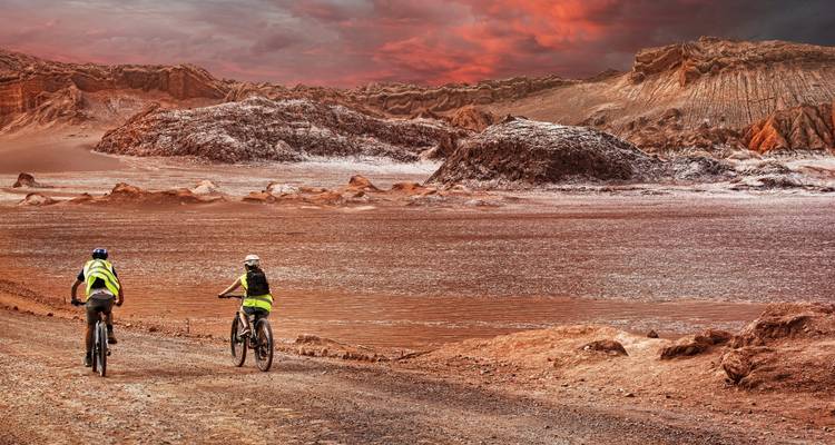 Radfahrer fahren durch unwirklich rotes Wüstenterrain unter dramatischem Himmel