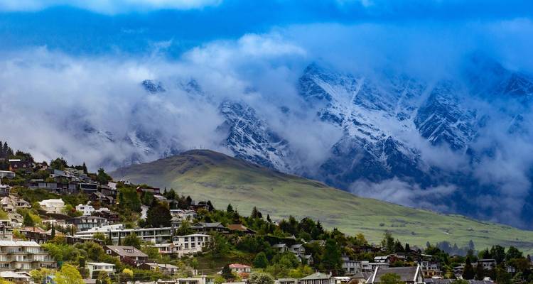 Les nuages tourbillonnent autour des sommets enneigés au-dessus d'une ville au bord du lac avec des maisons en terrasses qui grimpent sur le flanc de la colline.
