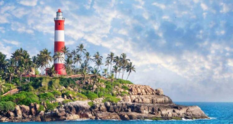 Rood-witte vuurtoren omringd door palmbomen aan een rotsachtige kustlijn van Kerala