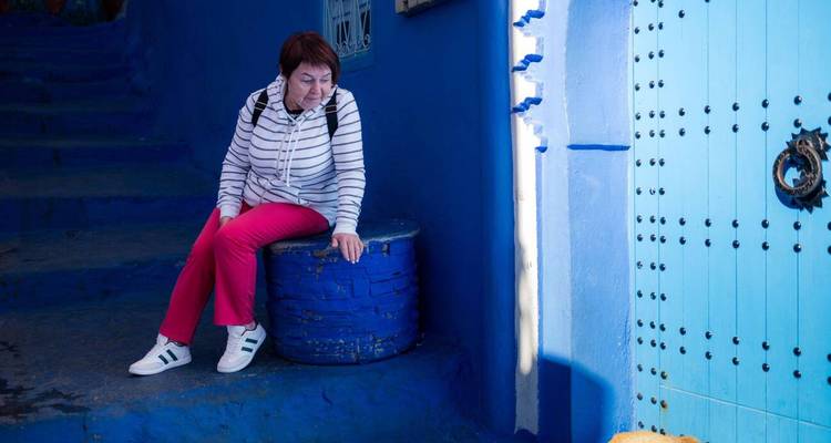 Femme en vêtements colorés se reposant sur un tonneau bleu dans les ruelles bleu vif de Chefchaouen