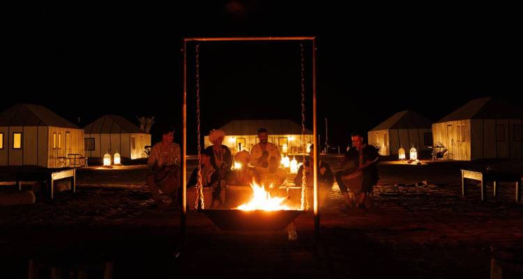 Des voyageurs rassemblés autour d'un feu de camp rougeoyant la nuit dans un campement de tentes du désert du Sahara