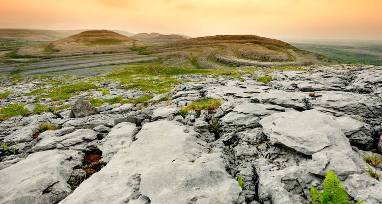 Kalksteinpflaster des Burren, das sich in goldene Hügel unter einem warmen Morgenhimmels erstreckt