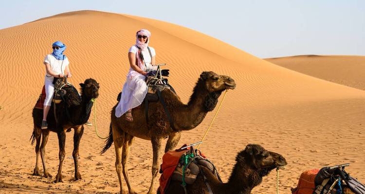 Deux voyageurs en foulards traditionnels chevauchant des chameaux à travers les dunes dorées du Sahara