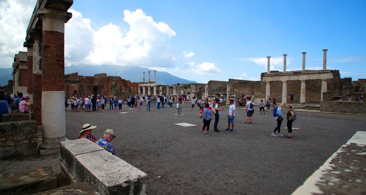 Amplio foro de Pompeya lleno de visitantes, con el Monte Vesubio al fondo.