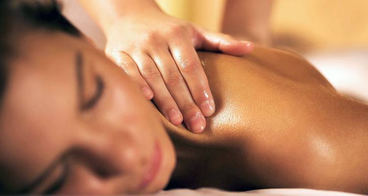 Gros plan sur les mains d'un masseur massant délicatement l'épaule huilée d'une femme.