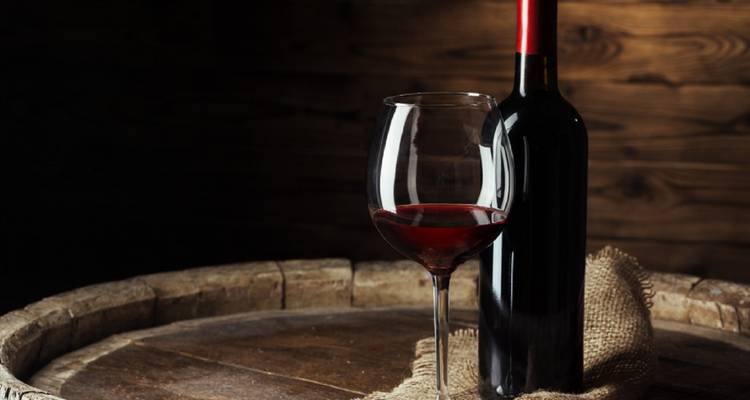 Nature morte d'une bouteille de vin rouge et d'un verre sur un fond de bois rustique.