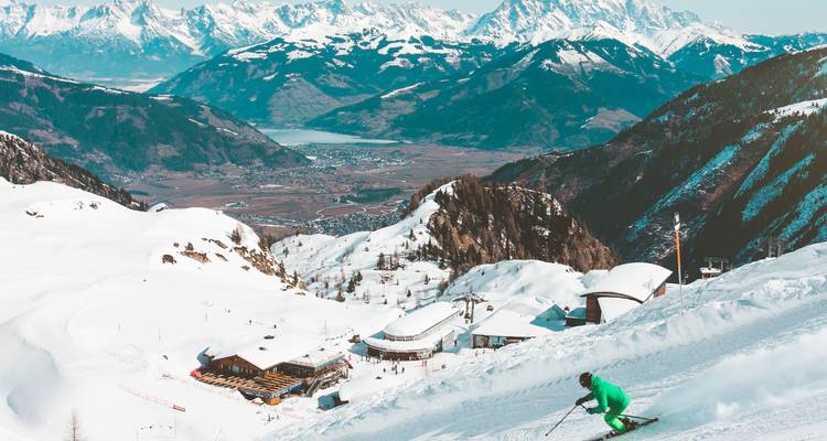 Skifahrer, der einen verschneiten Alpenhang hinunterschneidet mit panoramischen österreichischen Bergen und Tal darunter.
