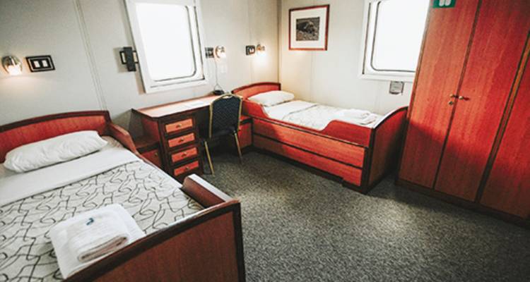 Compact twin cabin with two single beds, desk and window aboard a cruise vessel.