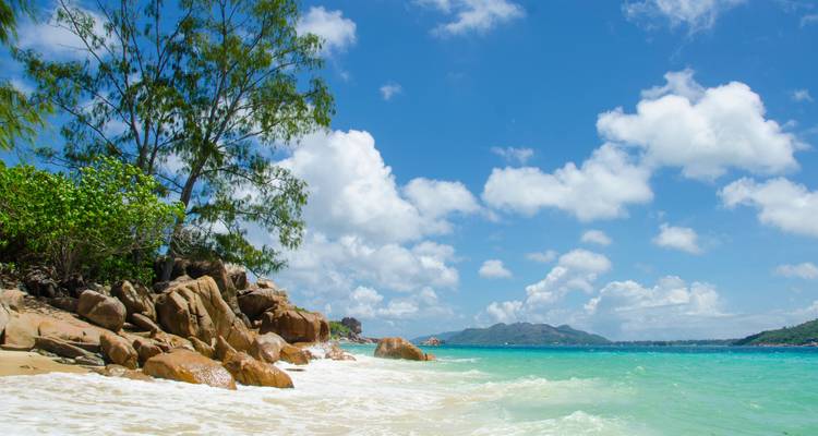 Tropische Küstenlinie mit türkisfarbenen Wellen, Felsvorsprüngen und vereinzelten Wolken am Himmel.