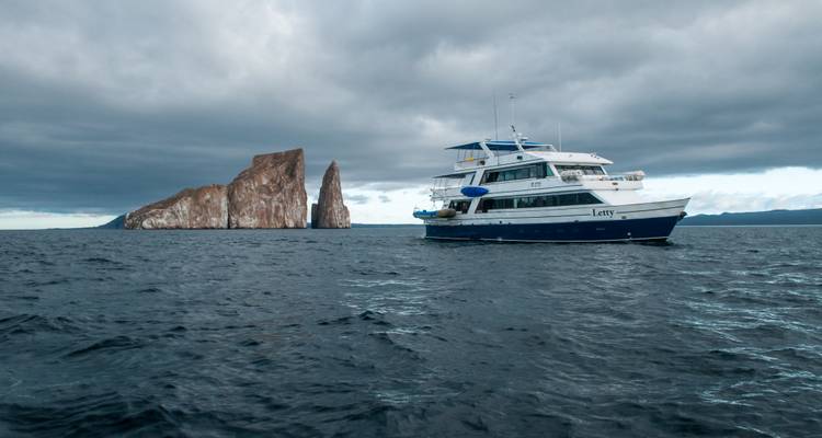 Cruise yacht anchored near the dramatic rock formation of Kicker Rock rising from the Pacific.
