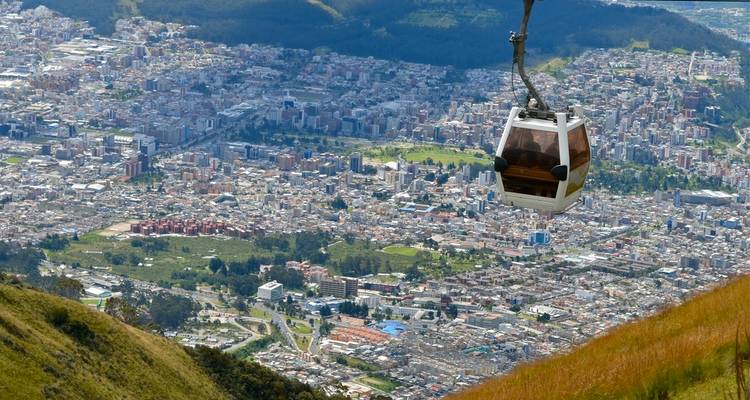 Gondola cabin ascending above Quito with sprawling city and Andean hills below.