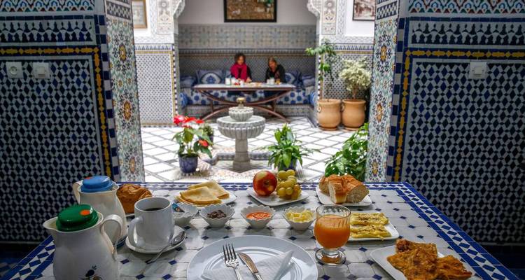 Petit-déjeuner marocain traditionnel étalé sur une table carrelée dans la cour d'un riad décoratif.