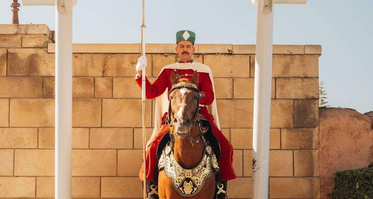 Garde marocain en uniforme à cheval se tenant à un poste cérémoniel contre un mur de pierre.