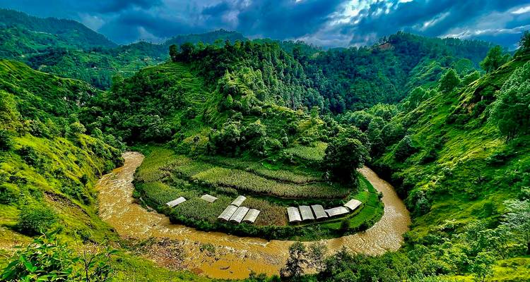 Vista aérea dramática de un valle verde donde un río marrón se curva alrededor de campos en terrazas bajo cielos tormentosos.