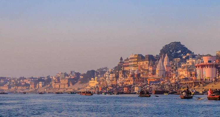 La suave luz vespertina baña los ghats de Varanasi a lo largo del Ganges mientras los barcos salpican el río en calma.
