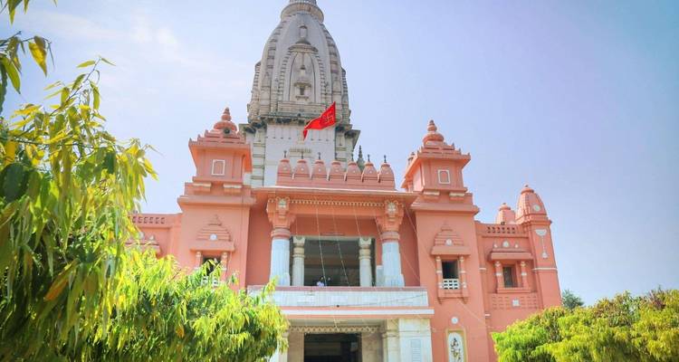 Un templo hindú de tonos rosados se alza contra un cielo despejado, enmarcado por follaje verde.