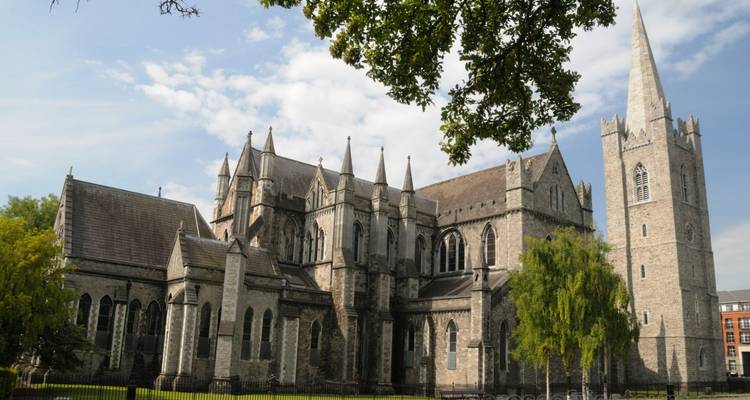 Stone Gothic cathedral with soaring spire and arched windows under a partly cloudy sky.