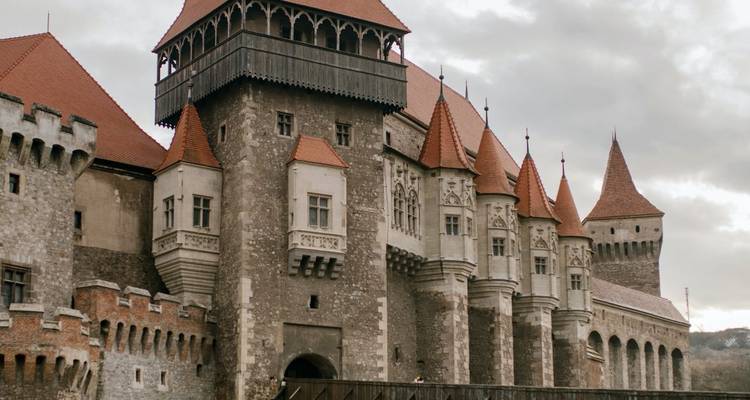 Impressive medieval castle with tall red-tiled towers and stone walls set against a moody sky.