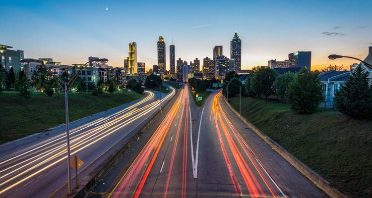 Nightfall cityscape with light trails on a highway leading toward a modern skyline and twilight sky.