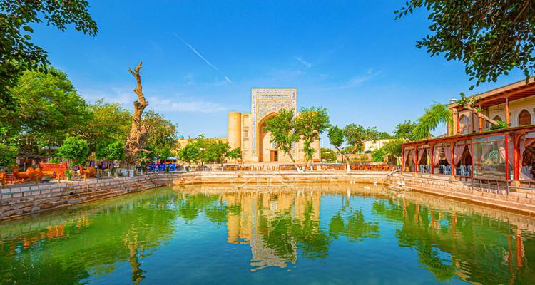 Bassin Lyabi Hauz reflétant l'architecture ancienne de Boukhara et les arbres feuillus sous un ciel dégagé