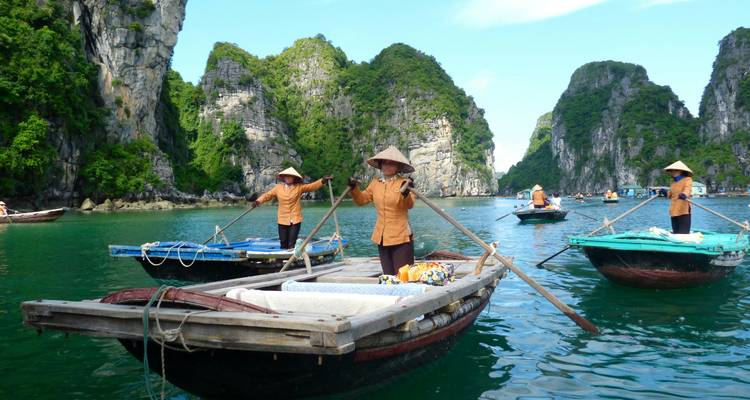 Traditional rowboats steered by standing oarsmen in conical hats on jade waters among karst cliffs.