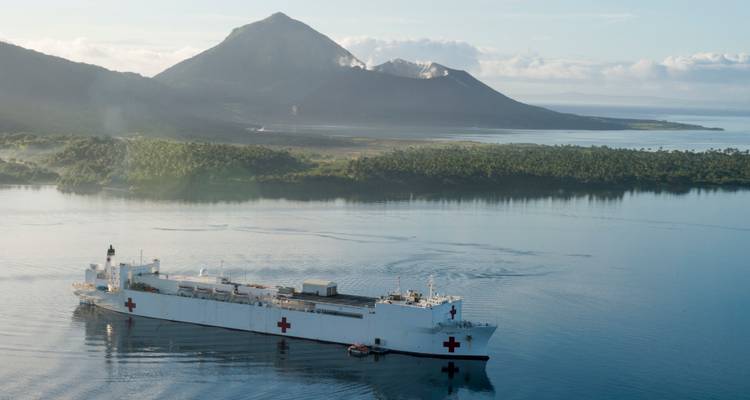 White hospital ship anchored in a calm bay with volcanic peaks in the distance